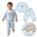 Uśmiechnięte dziecko w jasnoniebieskim chłopięcym dresie z motywem dinozaura marki PanPan 35 – idealny zestaw dresowy dla dzieci na co dzień. Prezentowana osobno bluza i spodnie wykonane z bawełny sprawiają, że ten strój do przedszkola jest zarówno praktyczny, jak i pełen radości. Zbliżenie ukazuje rysunkowego stegozaura z napisem „TEGOSAURUS” poniżej, co stanowi zabawny detal tego uroczego modelu bluzy z dinozaurem.