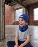 Śmiejący się chłopiec w zestawie czapka beanie i komin siedzi na podłodze w hali.