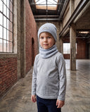 Chłopiec w zestawie czapka beanie i komin stoi w hali i patrzy w obiektyw.