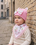 Dziewczynka w komplecie Flora w kolorze Baby pink siedzi oparta o ceglany mur.