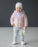 Młoda dziewczyna uśmiecha się w pomieszczeniu na jasnej podłodze, trzymając zabawkę królika i nosząc zestaw PanPan 35 czapka z uszami królika i chustą dla dziewczynki (bawełna, kwiatowy nadruk, wiosna). Tłem jest zwykła ciemnoszara ściana.